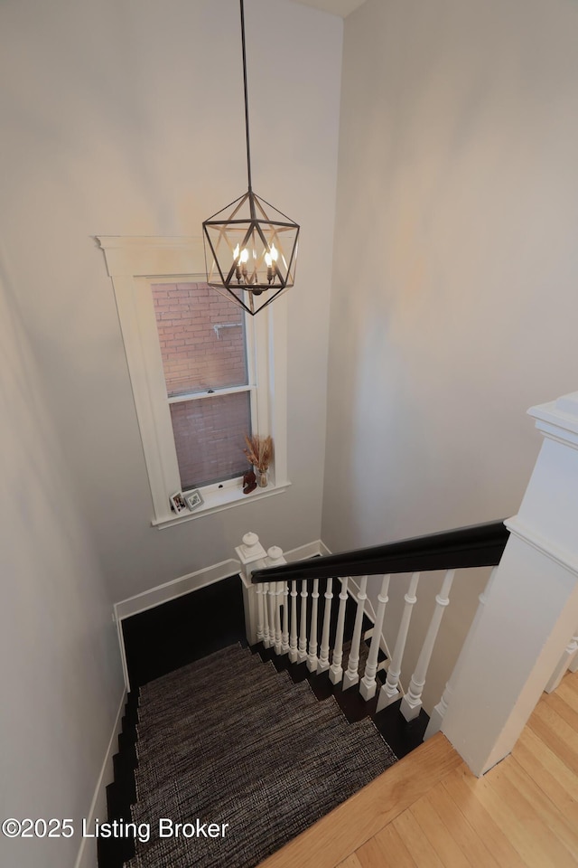 stairway with baseboards, a chandelier, and wood finished floors