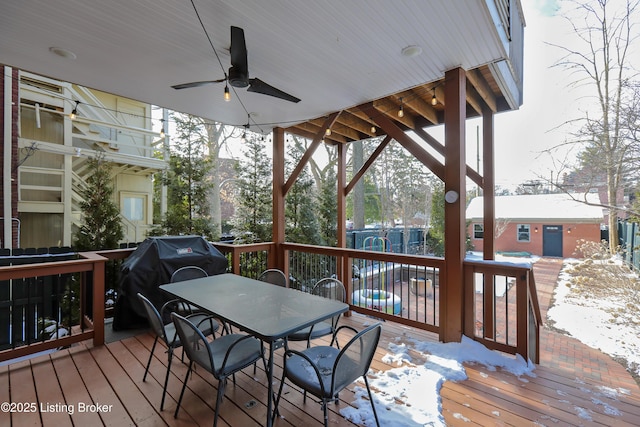 snow covered deck with ceiling fan, outdoor dining area, fence, grilling area, and a swimming pool