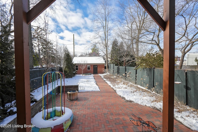 snow covered patio with a fenced backyard, a playground, and an outdoor structure