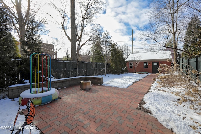 snow covered patio with an outbuilding, a fenced backyard, and a playground