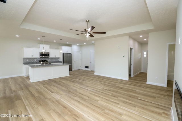 kitchen with an island with sink, a tray ceiling, stainless steel appliances, and open floor plan