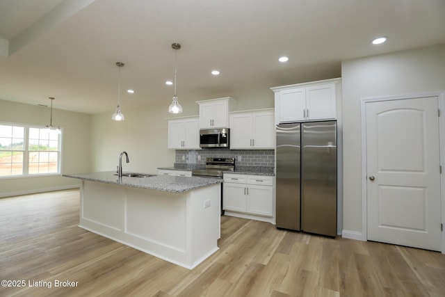 kitchen featuring a sink, white cabinetry, appliances with stainless steel finishes, an island with sink, and decorative light fixtures