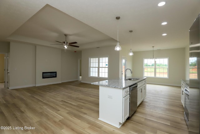 kitchen featuring an island with sink, light stone counters, open floor plan, stainless steel dishwasher, and a sink