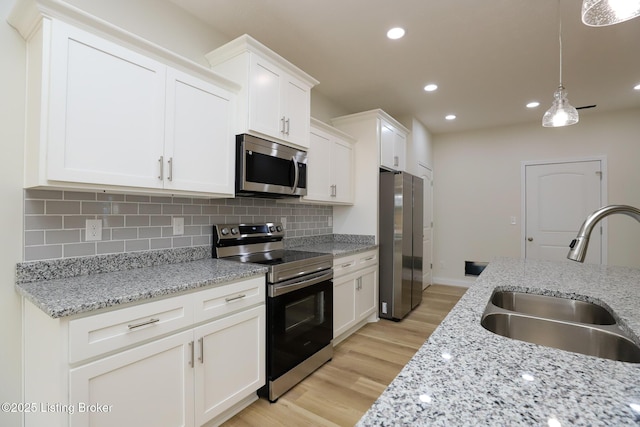 kitchen with a sink, white cabinetry, hanging light fixtures, appliances with stainless steel finishes, and light stone countertops