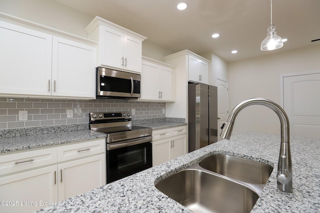 kitchen with appliances with stainless steel finishes, white cabinets, a sink, and tasteful backsplash