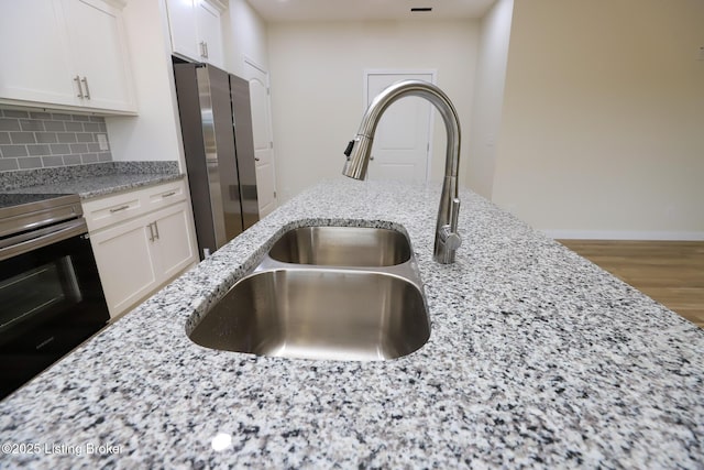 kitchen with appliances with stainless steel finishes, a sink, white cabinets, and light stone countertops