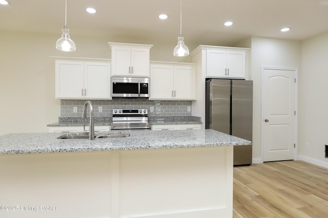 kitchen featuring pendant lighting, appliances with stainless steel finishes, white cabinets, a sink, and light stone countertops