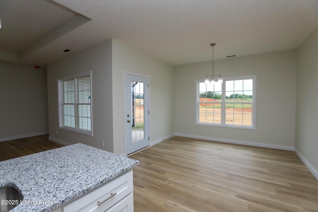 unfurnished dining area with baseboards, an inviting chandelier, and light wood-style floors