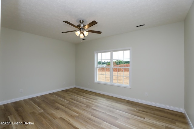 spare room with light wood-type flooring, baseboards, visible vents, and a textured ceiling