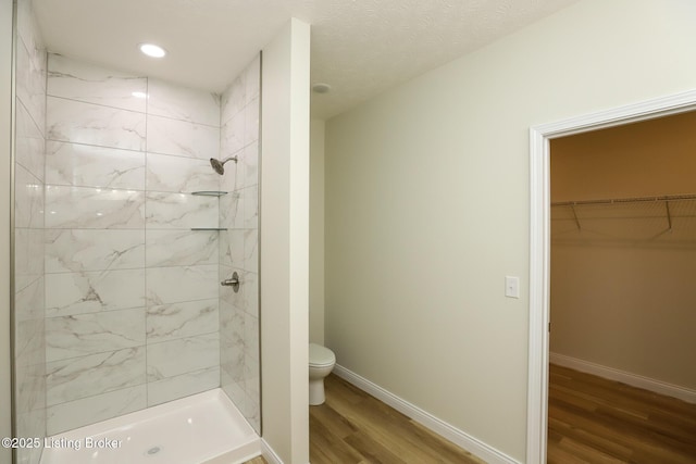 bathroom featuring a stall shower, baseboards, a walk in closet, and wood finished floors