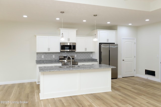 kitchen featuring appliances with stainless steel finishes, a center island with sink, decorative light fixtures, and white cabinets