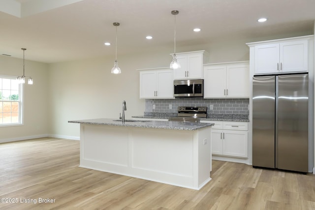 kitchen featuring a center island with sink, appliances with stainless steel finishes, decorative light fixtures, white cabinetry, and a sink