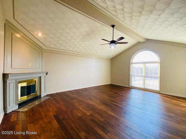 unfurnished living room with baseboards, lofted ceiling with beams, a fireplace with flush hearth, ornamental molding, and dark wood-type flooring