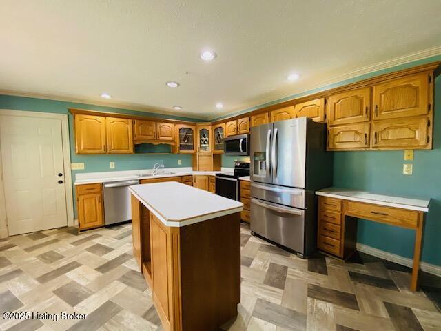 kitchen with brown cabinetry, glass insert cabinets, appliances with stainless steel finishes, light countertops, and a sink