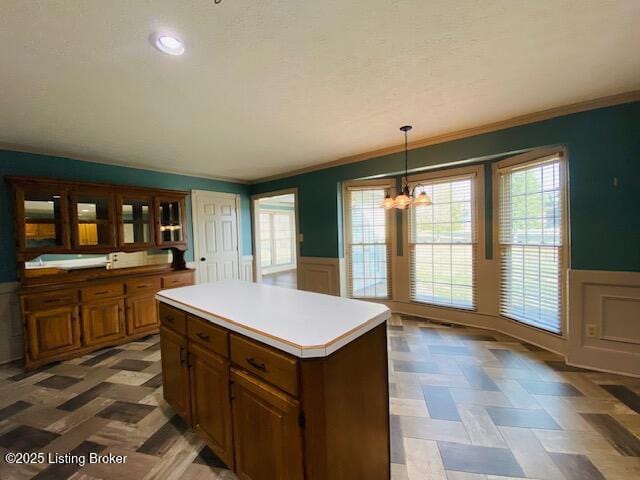 kitchen featuring light countertops, a center island, a wainscoted wall, and decorative light fixtures