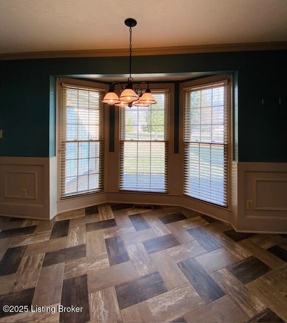 unfurnished dining area with ornamental molding, a wainscoted wall, and an inviting chandelier