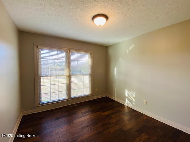 empty room featuring dark wood-style floors, visible vents, a textured ceiling, and baseboards