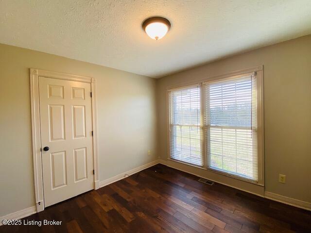 unfurnished room with dark wood-type flooring, a wealth of natural light, a textured ceiling, and baseboards