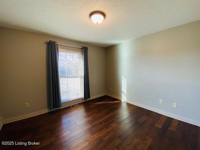 unfurnished room featuring dark wood-type flooring, visible vents, and baseboards