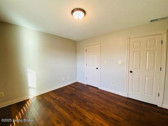 unfurnished bedroom featuring dark wood finished floors, visible vents, and baseboards