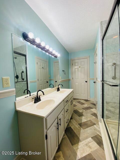 bathroom featuring double vanity, a stall shower, a textured ceiling, and a sink