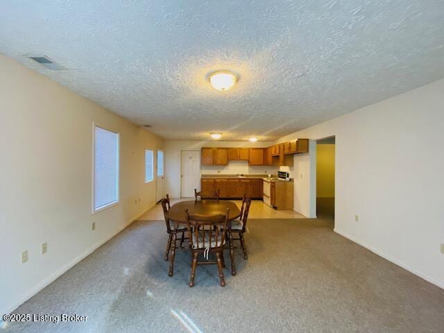 dining area featuring light carpet, baseboards, and a textured ceiling