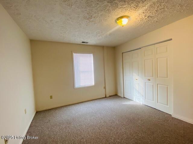 unfurnished bedroom with baseboards, visible vents, carpet, a textured ceiling, and a closet