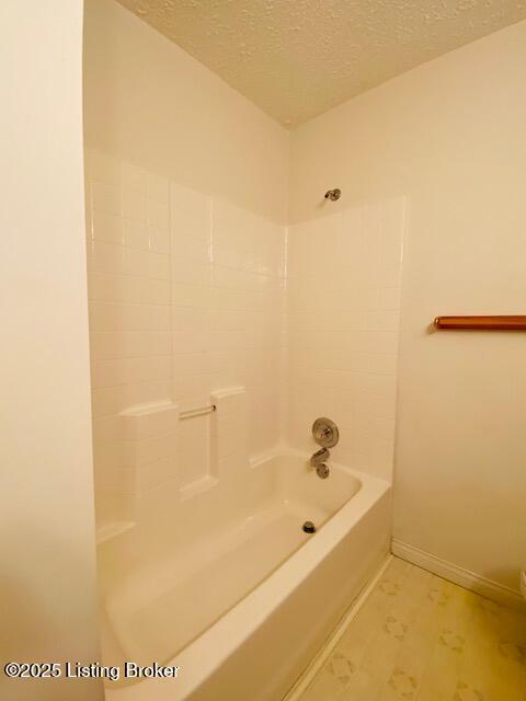 bathroom featuring bathtub / shower combination, a textured ceiling, and baseboards