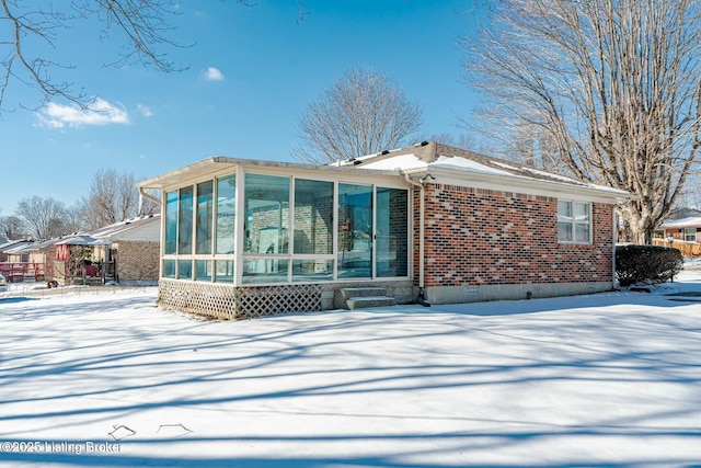 snow covered property featuring entry steps, a sunroom, and brick siding