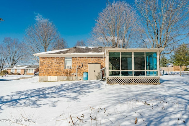 snow covered house featuring crawl space, a sunroom, and brick siding