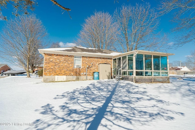 snow covered rear of property featuring a sunroom and brick siding