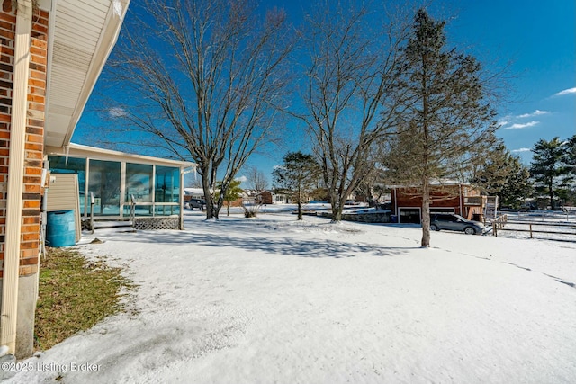 yard covered in snow featuring driveway, fence, and a sunroom