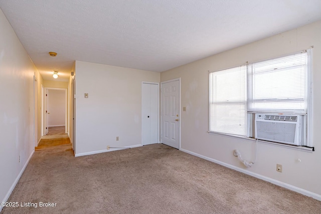 spare room featuring cooling unit, light carpet, a textured ceiling, and baseboards