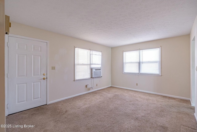 empty room featuring cooling unit, light carpet, a textured ceiling, and baseboards