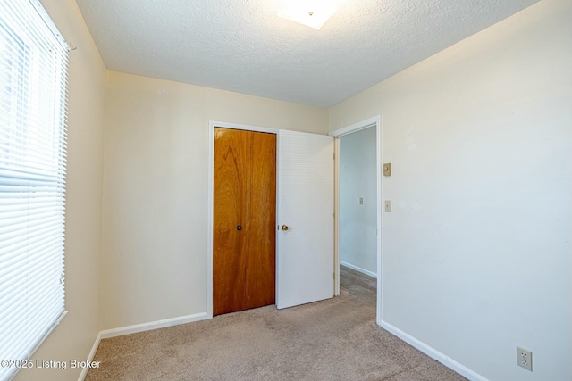 unfurnished bedroom featuring a closet, light colored carpet, a textured ceiling, and baseboards