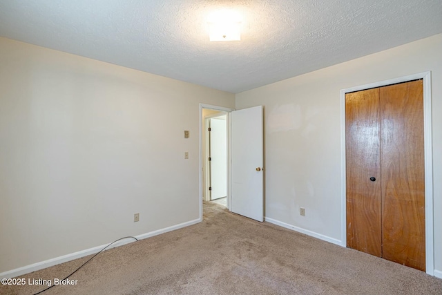 unfurnished bedroom with a closet, light colored carpet, a textured ceiling, and baseboards