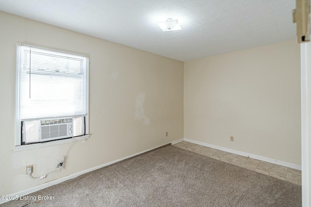 carpeted empty room featuring a textured ceiling, baseboards, and cooling unit