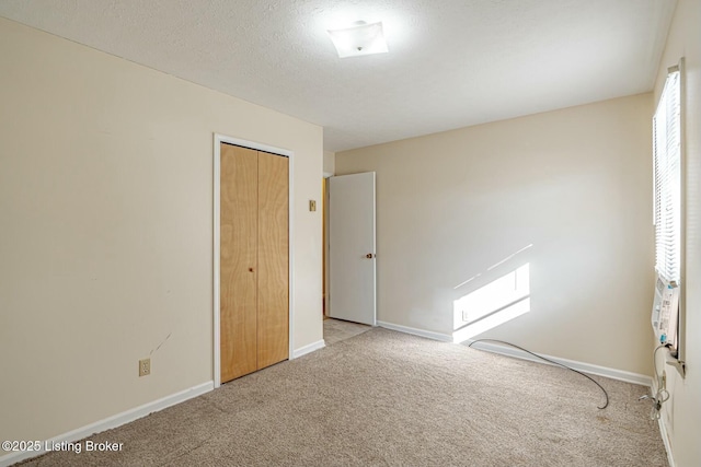 unfurnished bedroom featuring a textured ceiling, a closet, baseboards, and light colored carpet