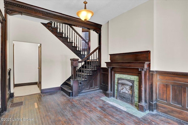 unfurnished living room featuring a wainscoted wall, a fireplace, visible vents, wood finished floors, and stairs