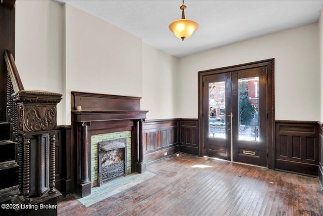 entrance foyer featuring a wainscoted wall, a fireplace with flush hearth, wood finished floors, and french doors