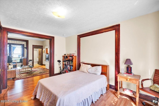 bedroom with connected bathroom, a textured ceiling, and wood finished floors