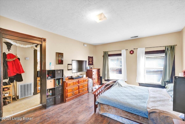 bedroom with a textured ceiling, visible vents, and wood finished floors