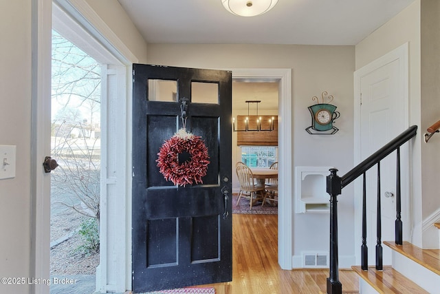 foyer with wood finished floors, visible vents, baseboards, and stairs