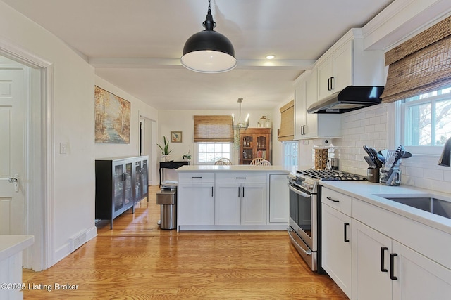 kitchen with decorative light fixtures, light countertops, white cabinets, a sink, and stainless steel gas range