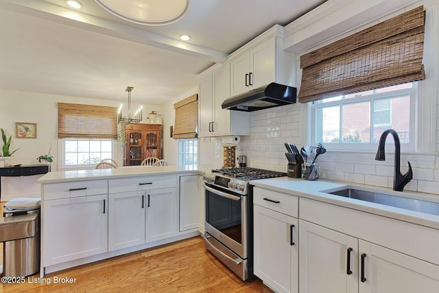 kitchen featuring under cabinet range hood, a sink, white cabinetry, light countertops, and stainless steel gas range