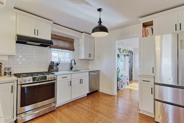 kitchen with stainless steel appliances, light countertops, under cabinet range hood, white cabinetry, and a sink