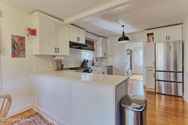 kitchen featuring under cabinet range hood, stainless steel appliances, white cabinets, light countertops, and decorative light fixtures