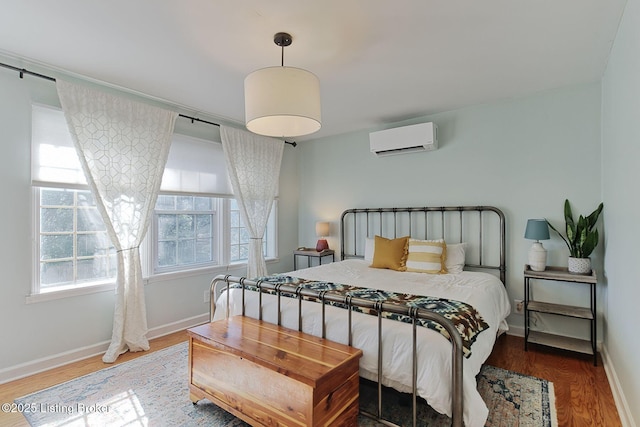 bedroom featuring a wall unit AC, multiple windows, baseboards, and wood finished floors