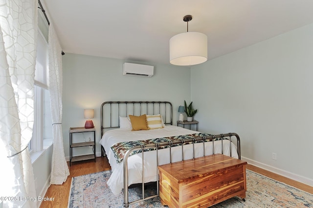 bedroom featuring baseboards, wood finished floors, and a wall mounted AC