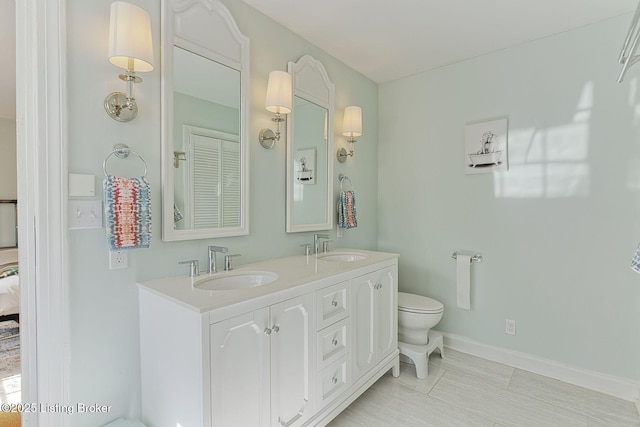 bathroom featuring toilet, double vanity, baseboards, and a sink